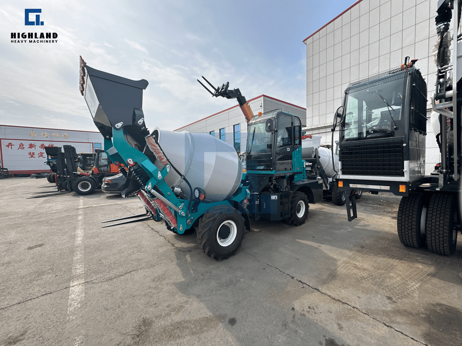 HIGHLAND HEAVY MACHINERY 1.5m³ compact self loading concrete mixer truck in teal blue with front lifting bucket, parked next to a large transport truck at a factory yard.
