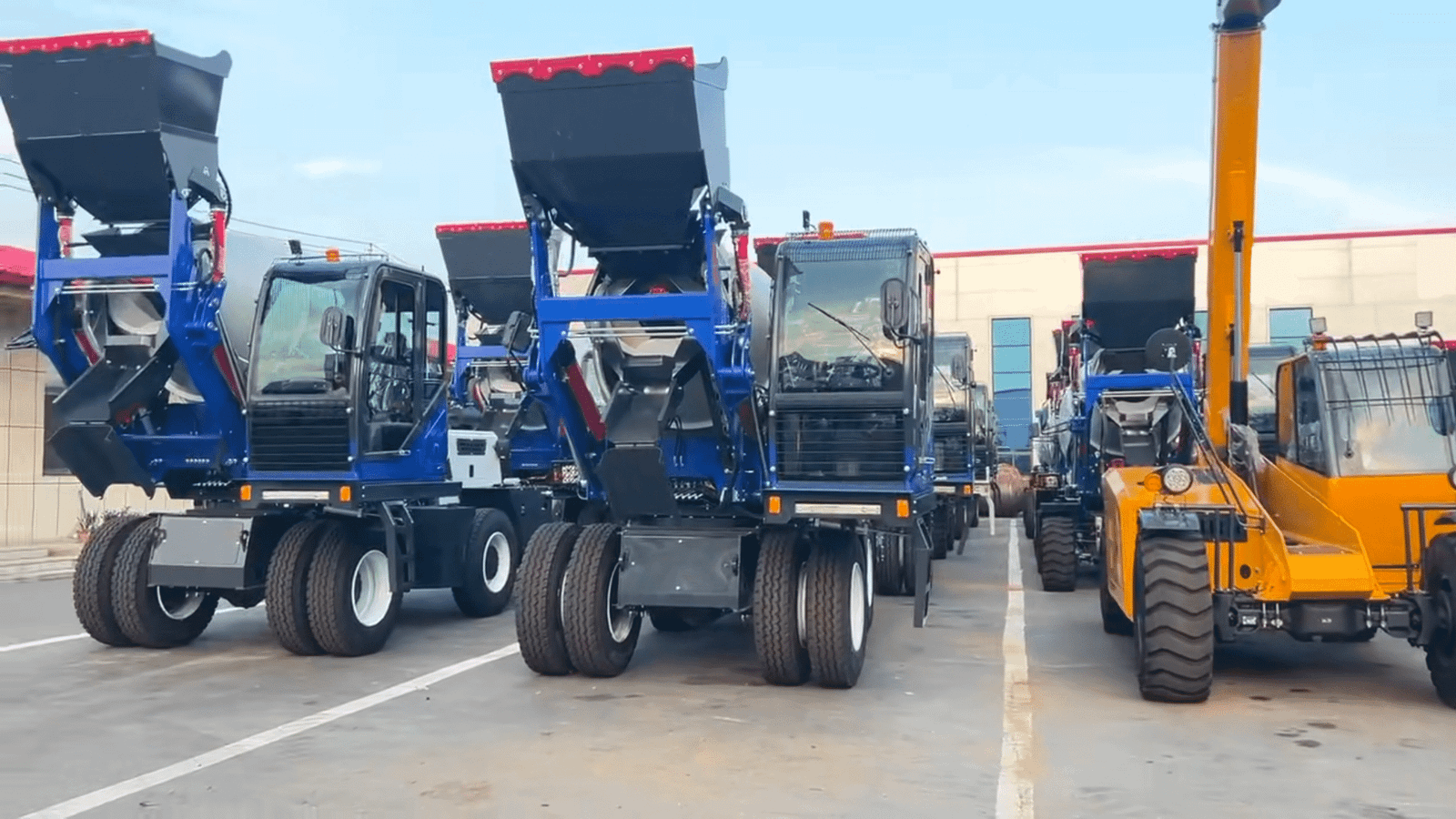 HIGHLAND HEAVY MACHINERY blue self loading concrete mixer trucks with raised hoppers lined up alongside a yellow rough terrain forklift in an outdoor factory yard, showcasing mixed-fleet production readiness for the Home page.