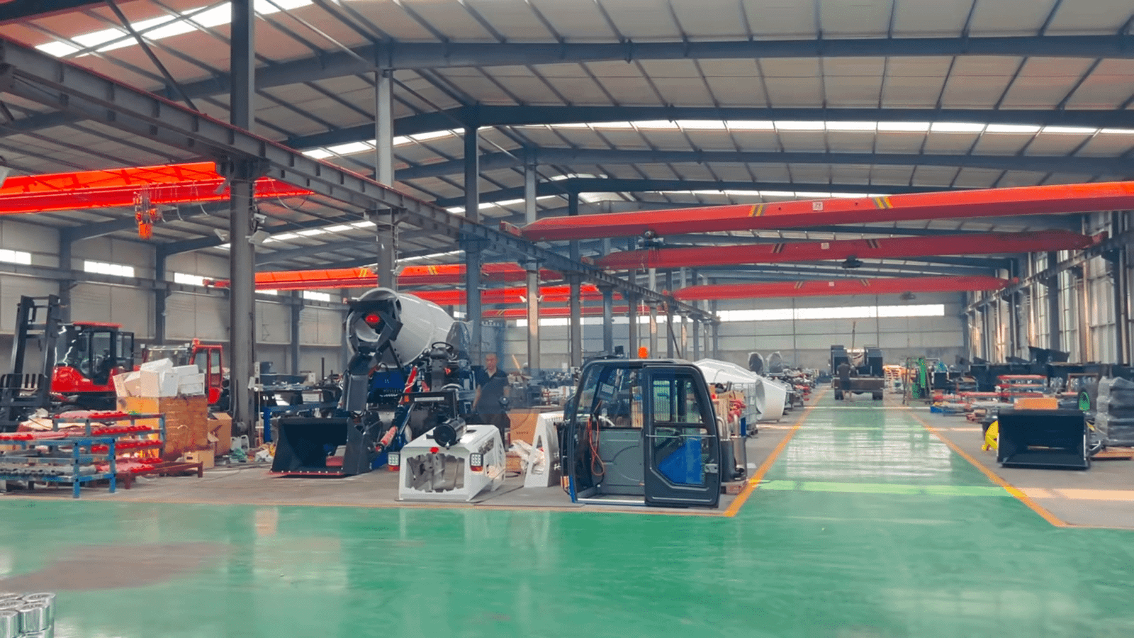 HIGHLAND HEAVY MACHINERY wide-angle factory production line with overhead red cranes, multiple assembly stations, cabins, chassis, and self-loading mixer trucks arranged along a green epoxy floor with yellow safety lines.