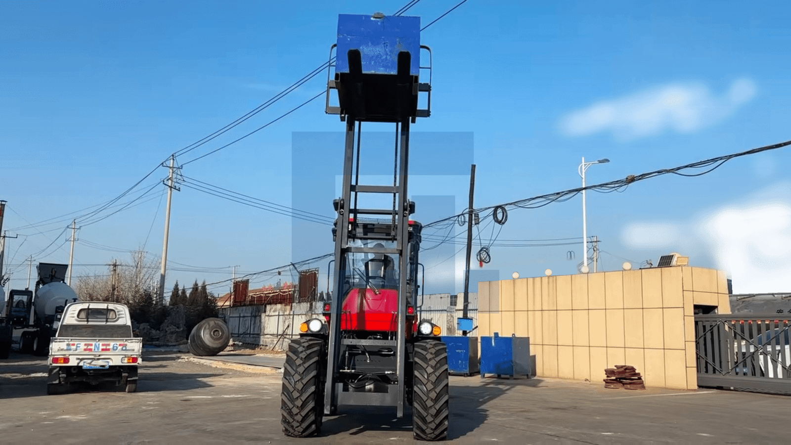 HIGHLAND HEAVY MACHINERY red rough terrain forklift front view with forks fully raised, carrying a blue load in a service yard, with a white truck and concrete mixer visible in the background.