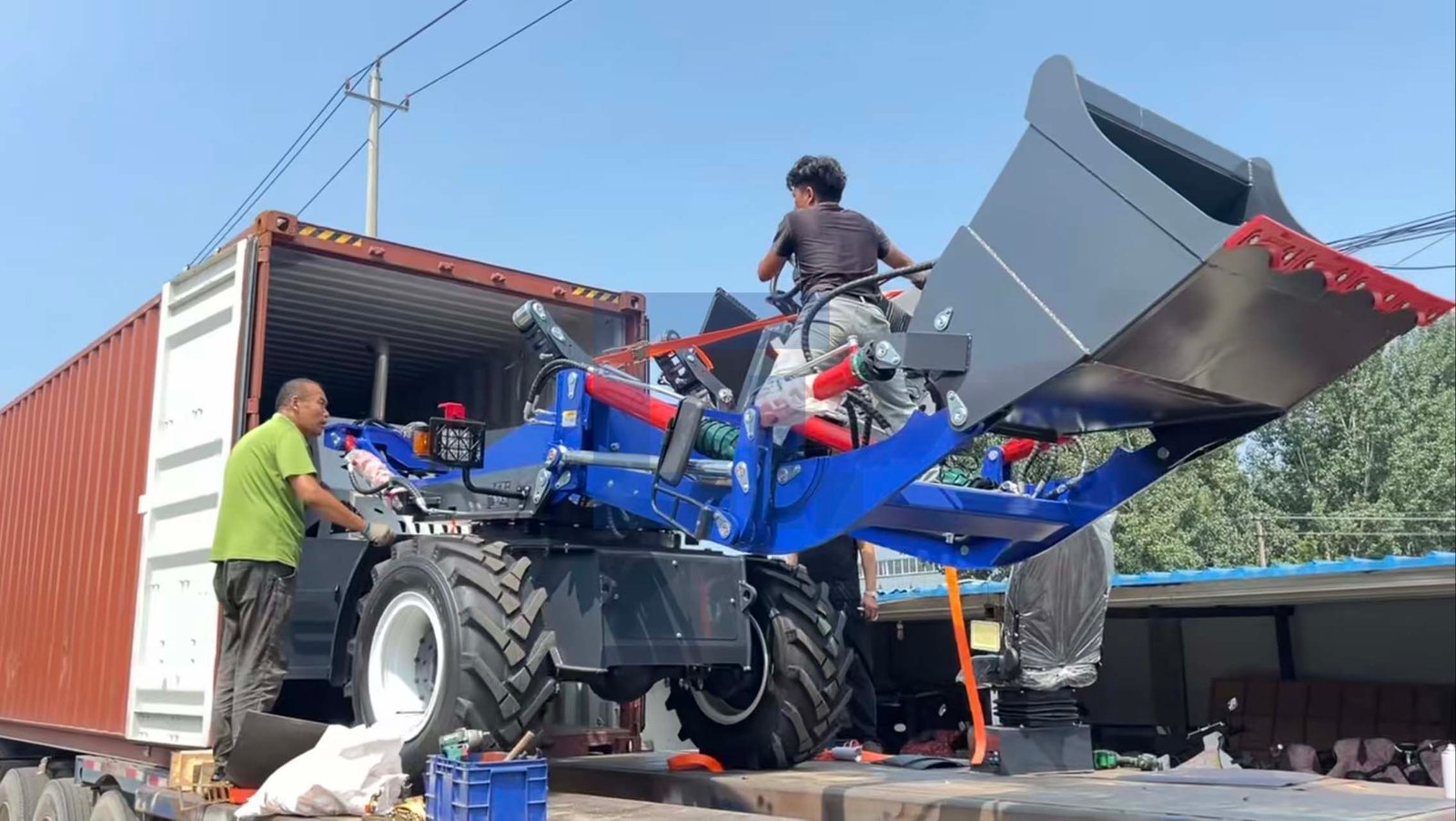HIGHLAND HEAVY MACHINERY blue mini wheel loader with raised bucket being carefully loaded into a shipping container by workers for global export, demonstrating secure logistics handling.