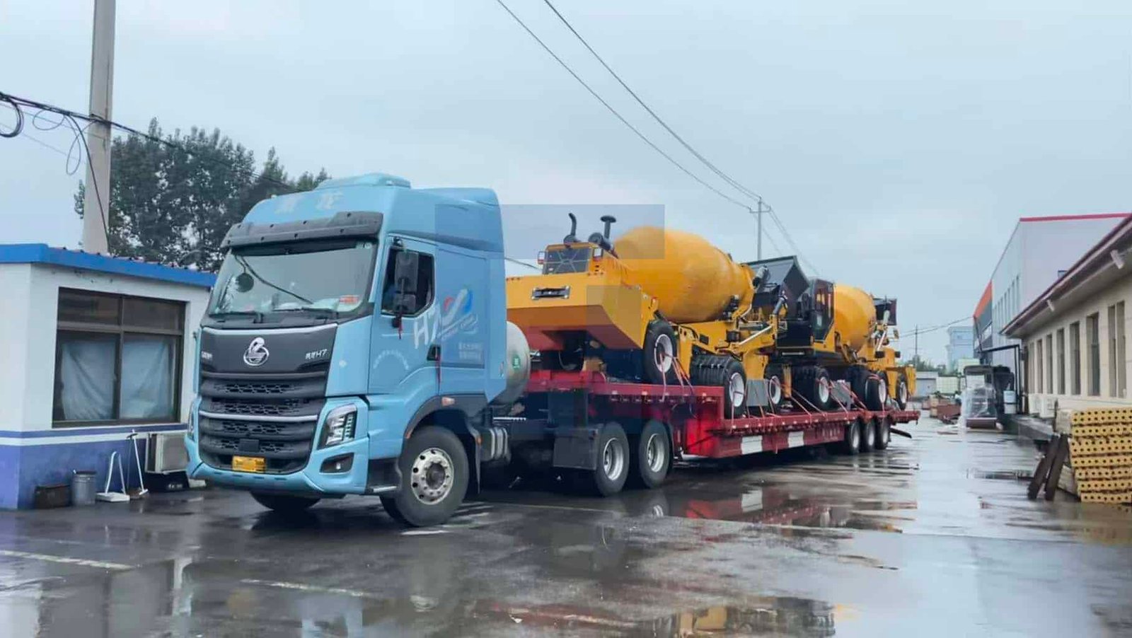 HIGHLAND HEAVY MACHINERY blue truck tractor pulling a red flatbed trailer loaded with multiple yellow self loading concrete mixer trucks, parked on a wet factory road after rain, ready for batch export.