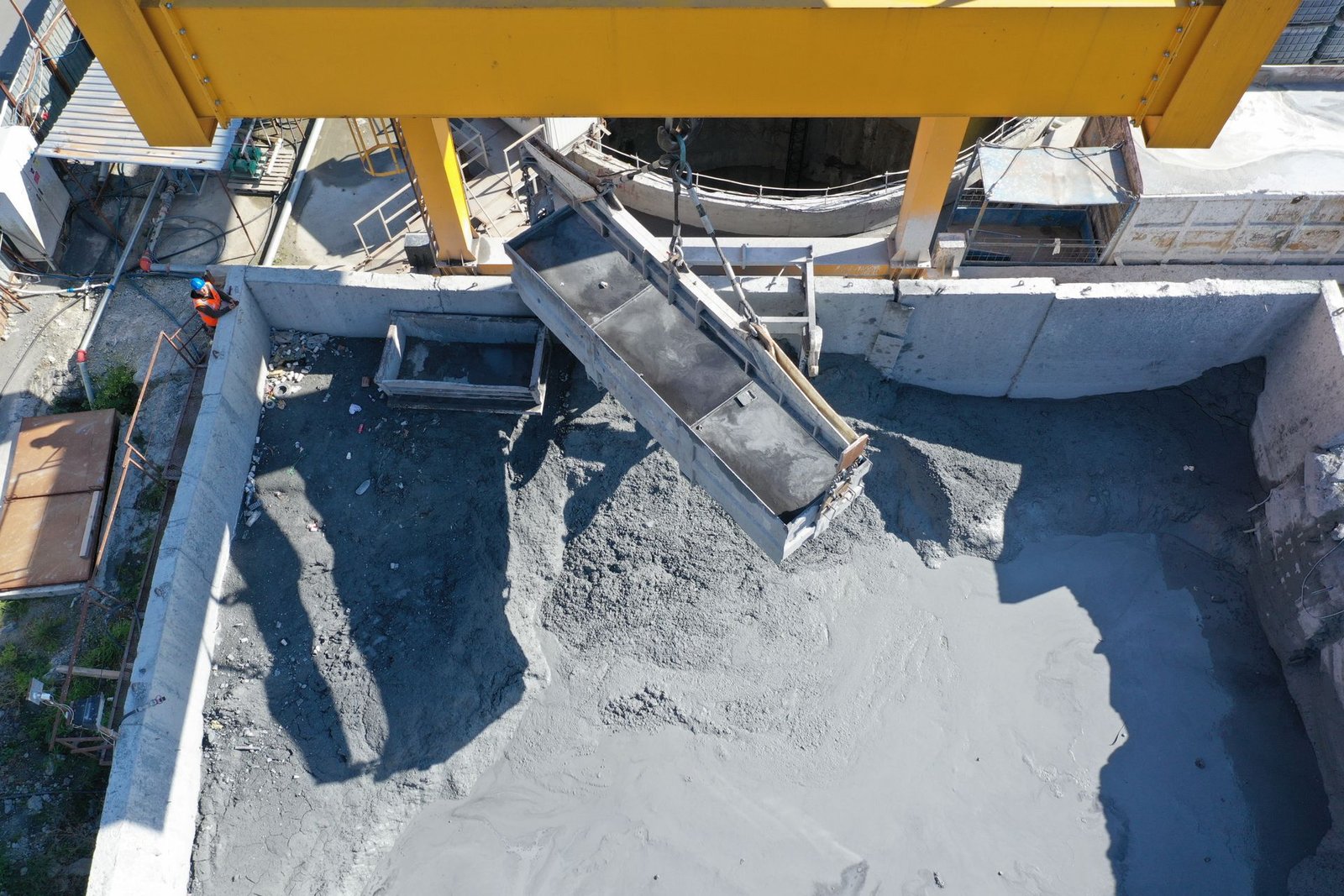 HIGHLAND HEAVY MACHINERY construction site scene showing freshly mixed concrete being poured from a crane bucket into a reinforced foundation trench, demonstrating efficient material placement and structural integrity on a large-scale project.