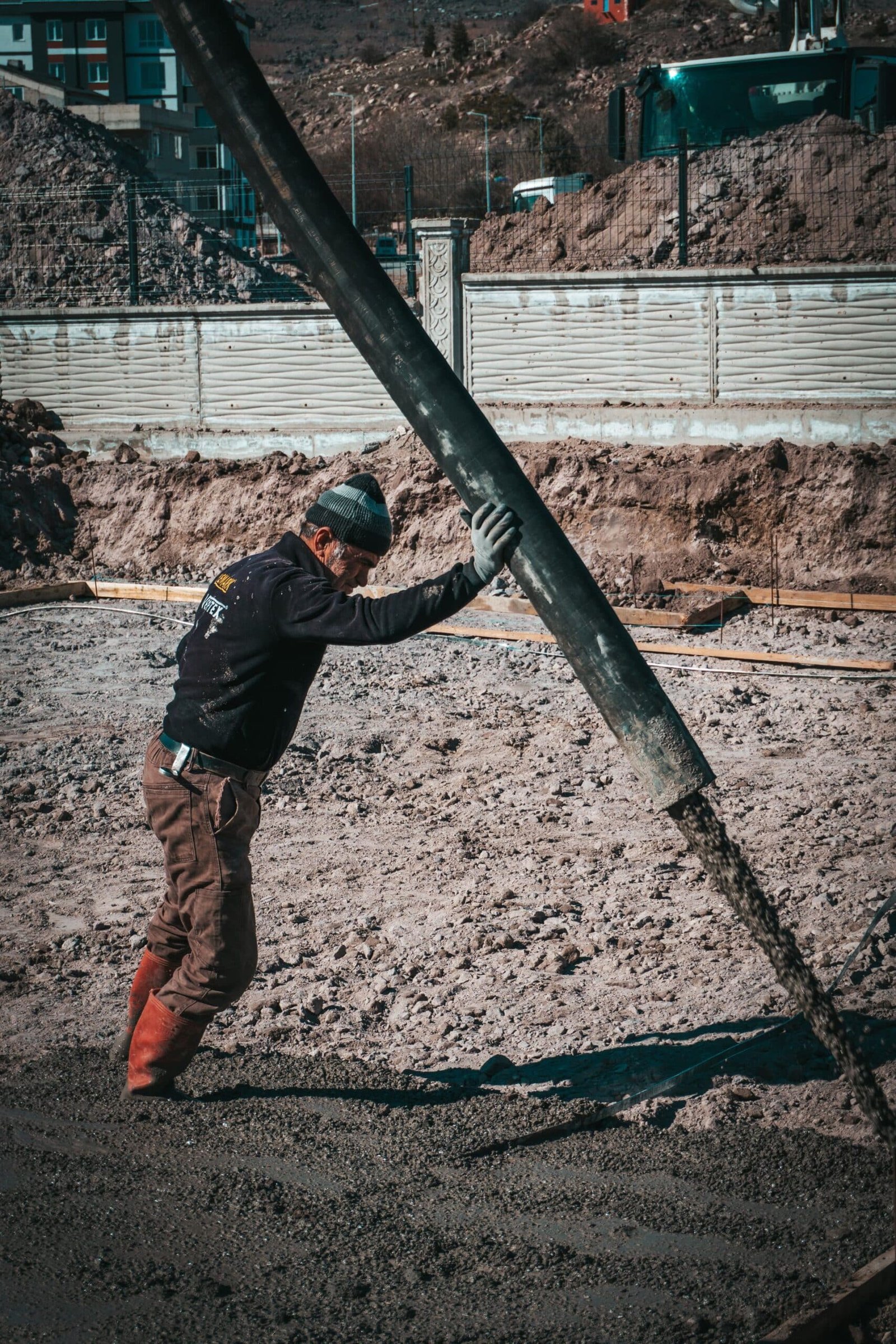 HIGHLAND HEAVY MACHINERY construction worker directing a heavy-duty concrete pump hose to pour wet concrete into a foundation trench on an active building site.