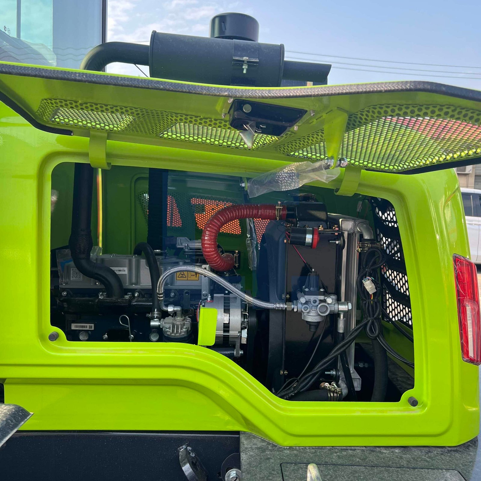 HIGHLAND HEAVY MACHINERY bright green heavy equipment engine compartment with open maintenance panel, showing a robust diesel engine, hydraulic pump, air intake hose, and protective film on brand new components.