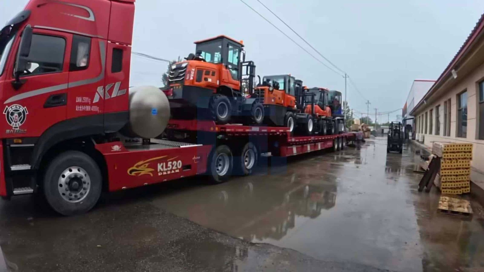 HIGHLAND HEAVY MACHINERY multiple orange rough terrain forklifts loaded on a red KL520 flatbed trailer, parked on a wet factory road after rain, ready for bulk shipment.