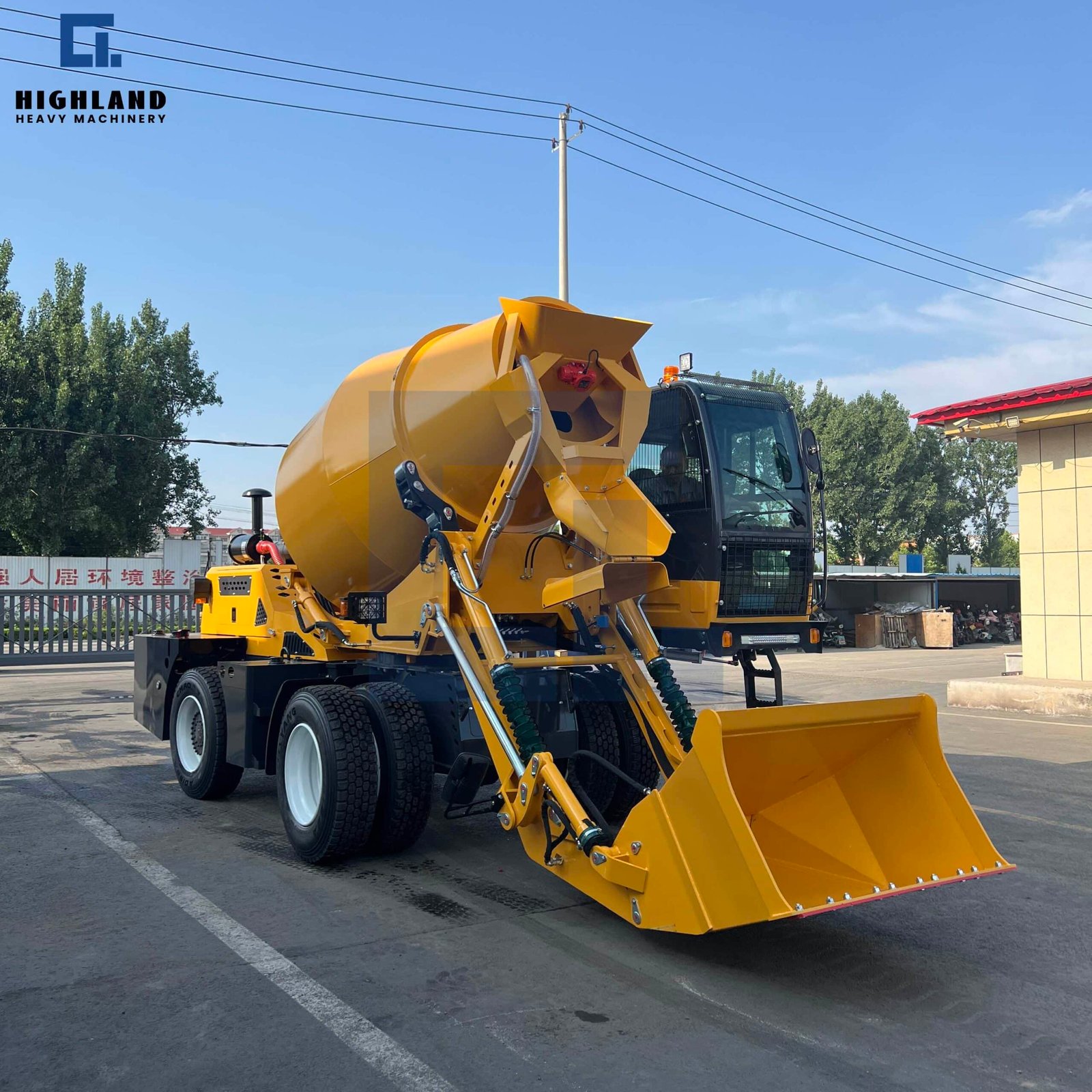 HIGHLAND HEAVY MACHINERY yellow self loading concrete mixer truck with loader bucket resting on the ground and mixing drum tilted back, parked in an industrial yard, ready for efficient material loading.